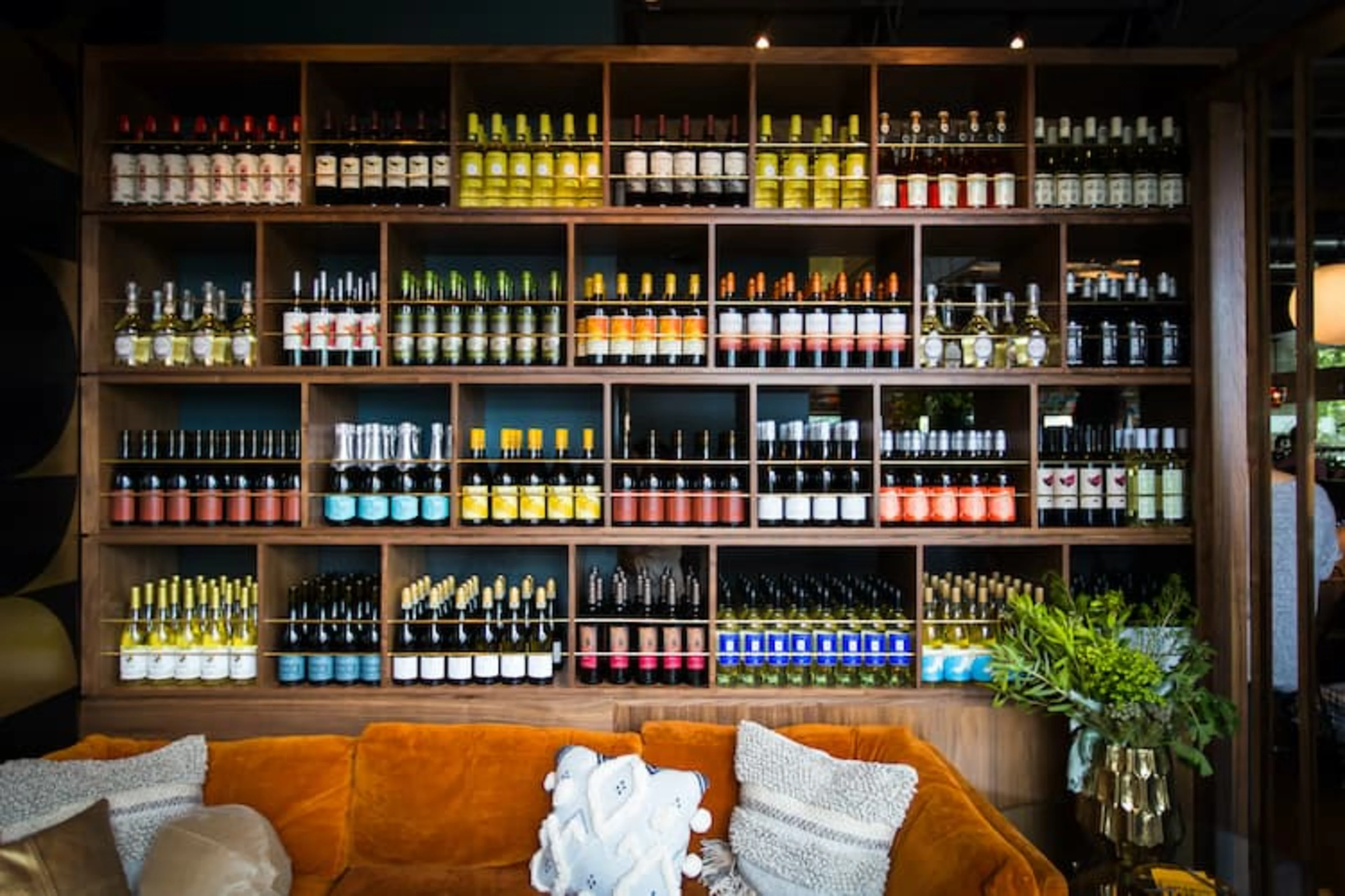 A large wine display on shelves above an orange couch.