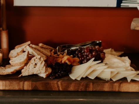 A wooden board covered in bread, cheese and fruits.
