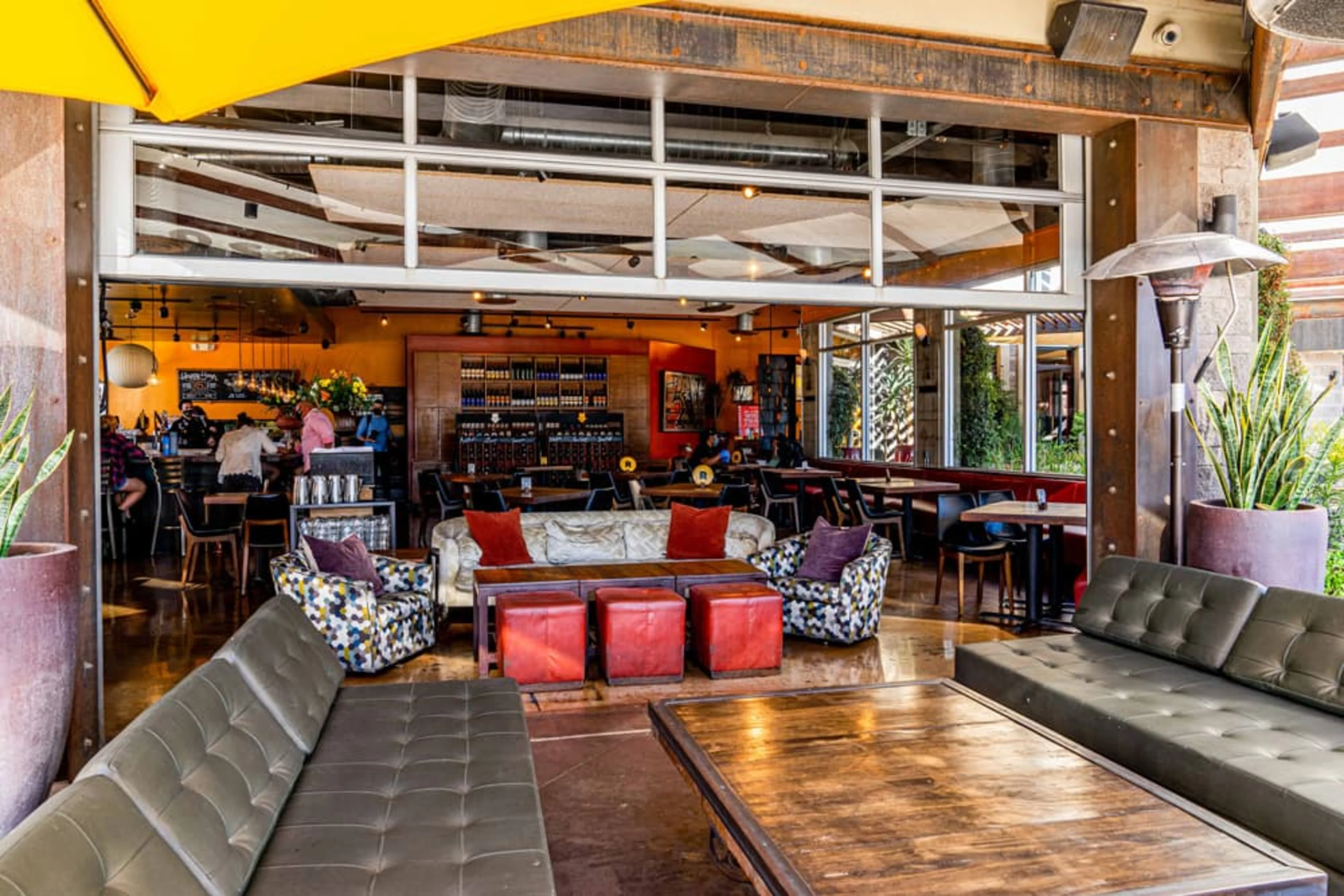 Postino patio with long grey sofas and wooden tables with red stools.