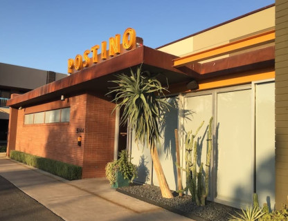 A building with desert plants outside and a large yellow Postino sign.