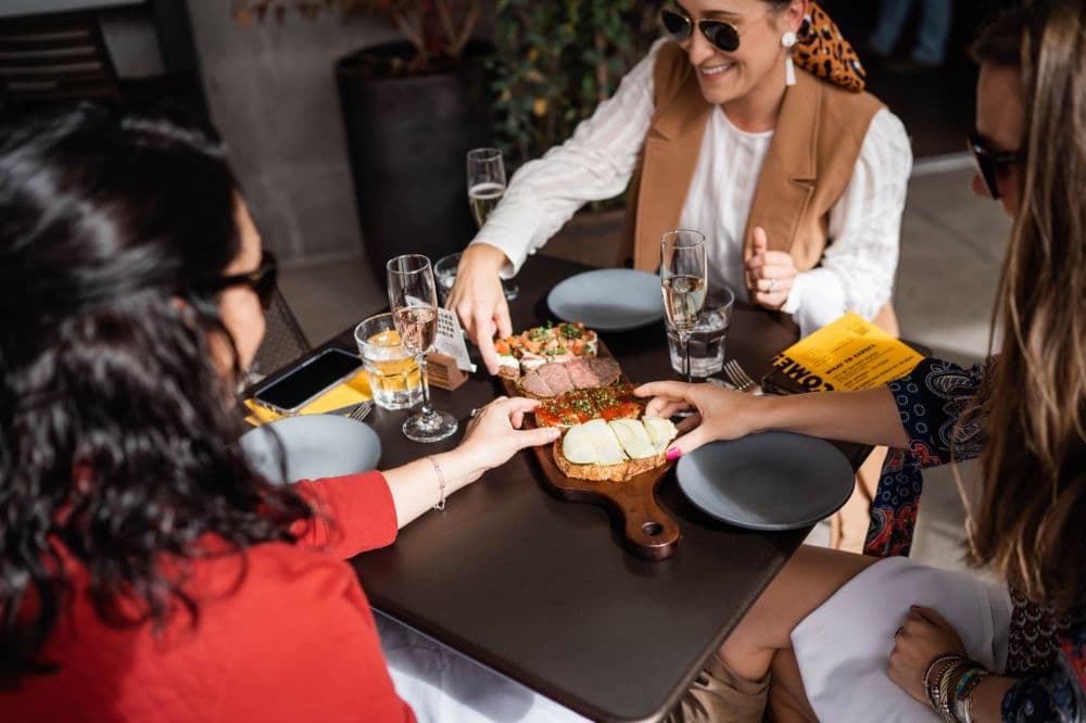 Three people sitting at a table sharing a wooden food board.