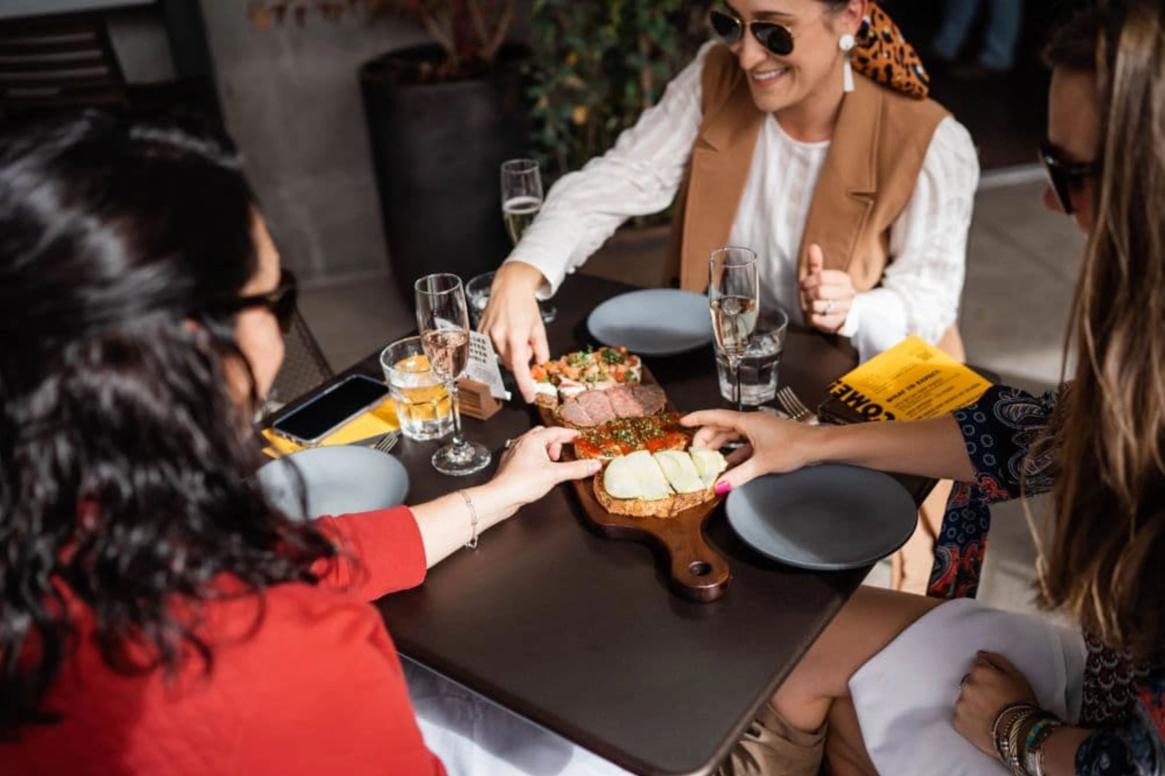 Three people sitting at a table sharing a wooden food board.