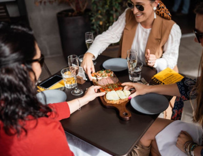 Three people sitting at a table sharing a wooden food board.
