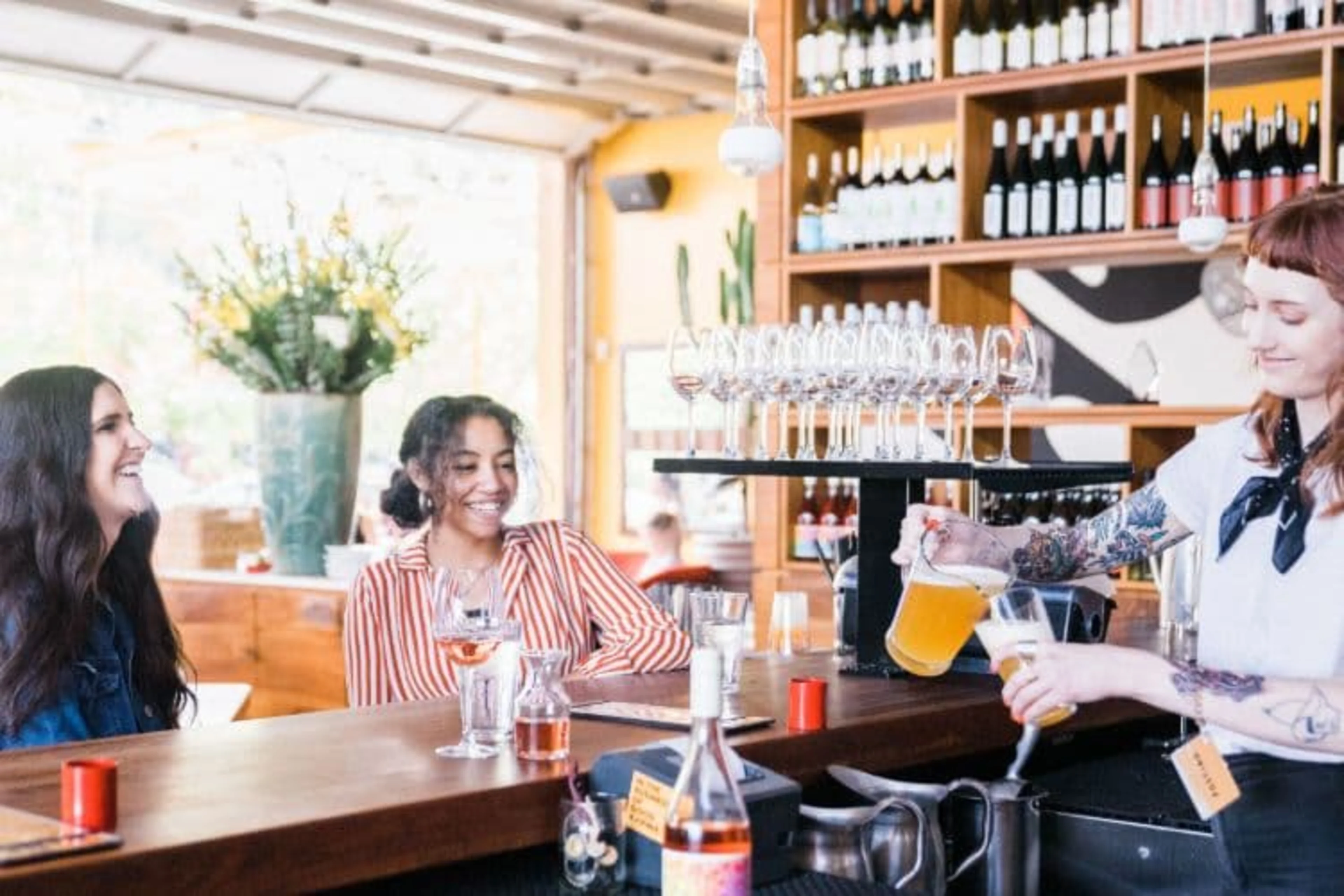 A bartender is pouring a pitcher of beer to two customers.