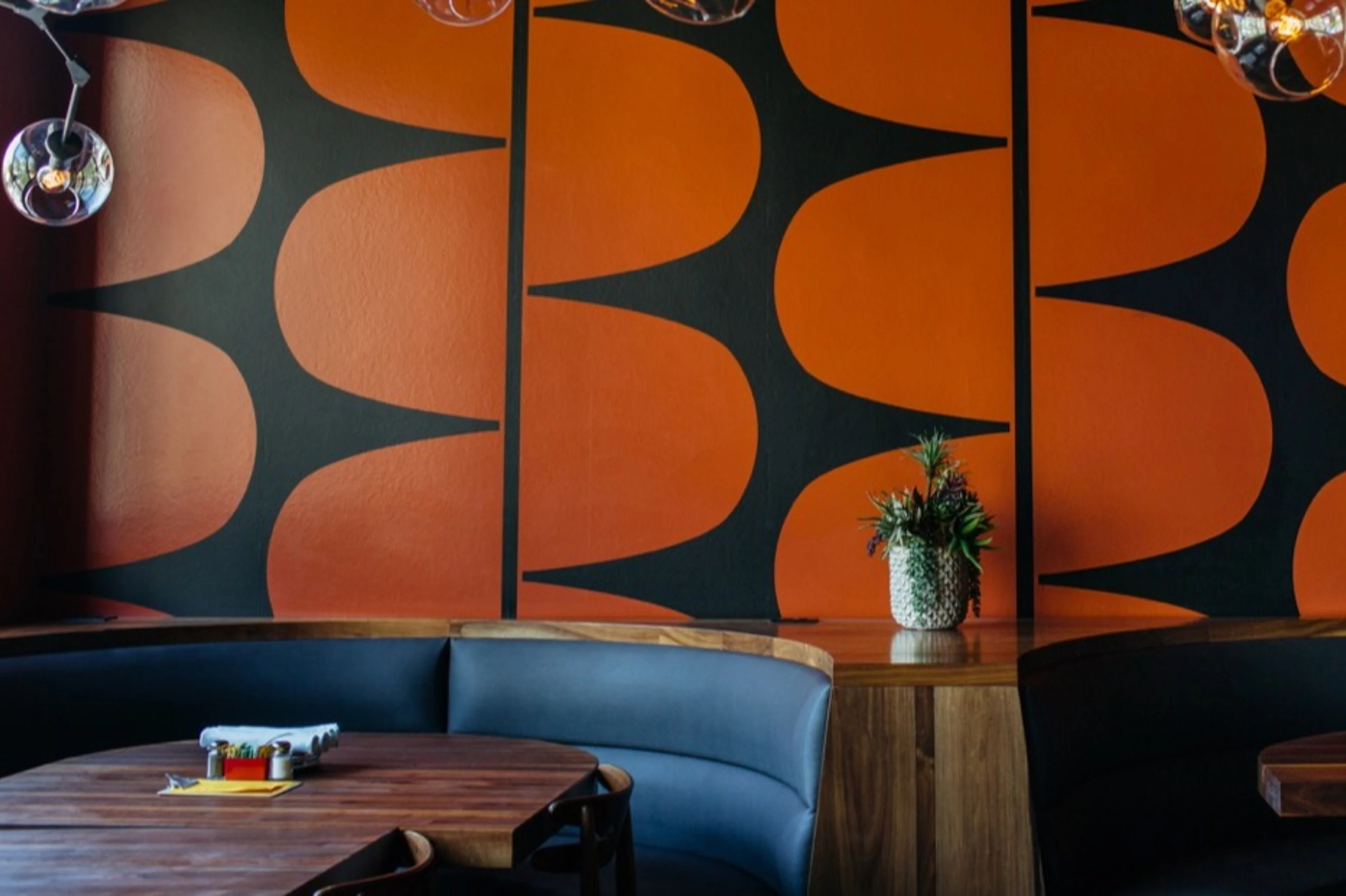 Grey booths with wooden tables and orange walls.