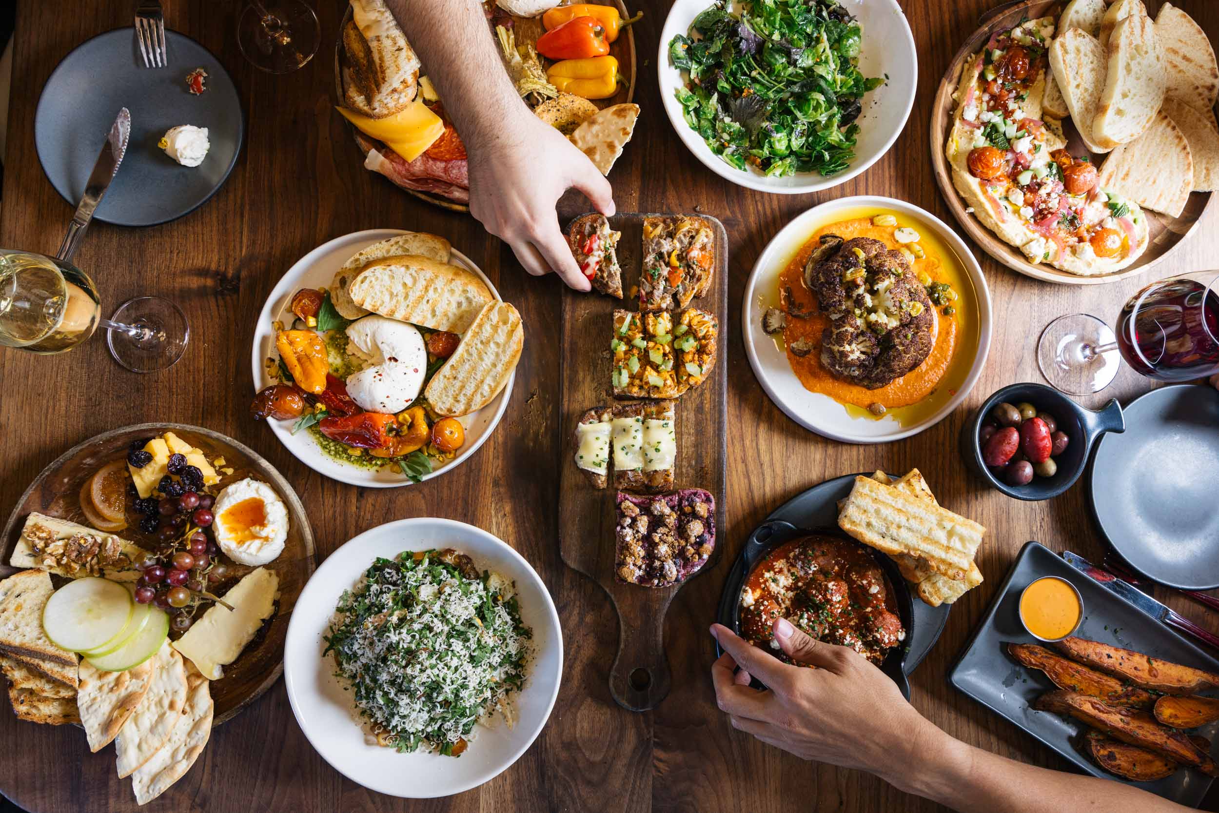 Overhead photo of Postino appetizers and hands reaching for food