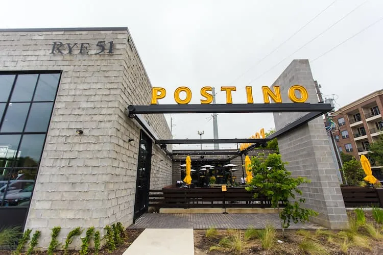 A white brick building with a large yellow Postino sign.