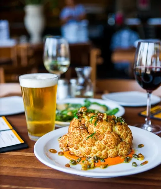 Roasted cauliflower on a plate with a beer and a glass of wine.