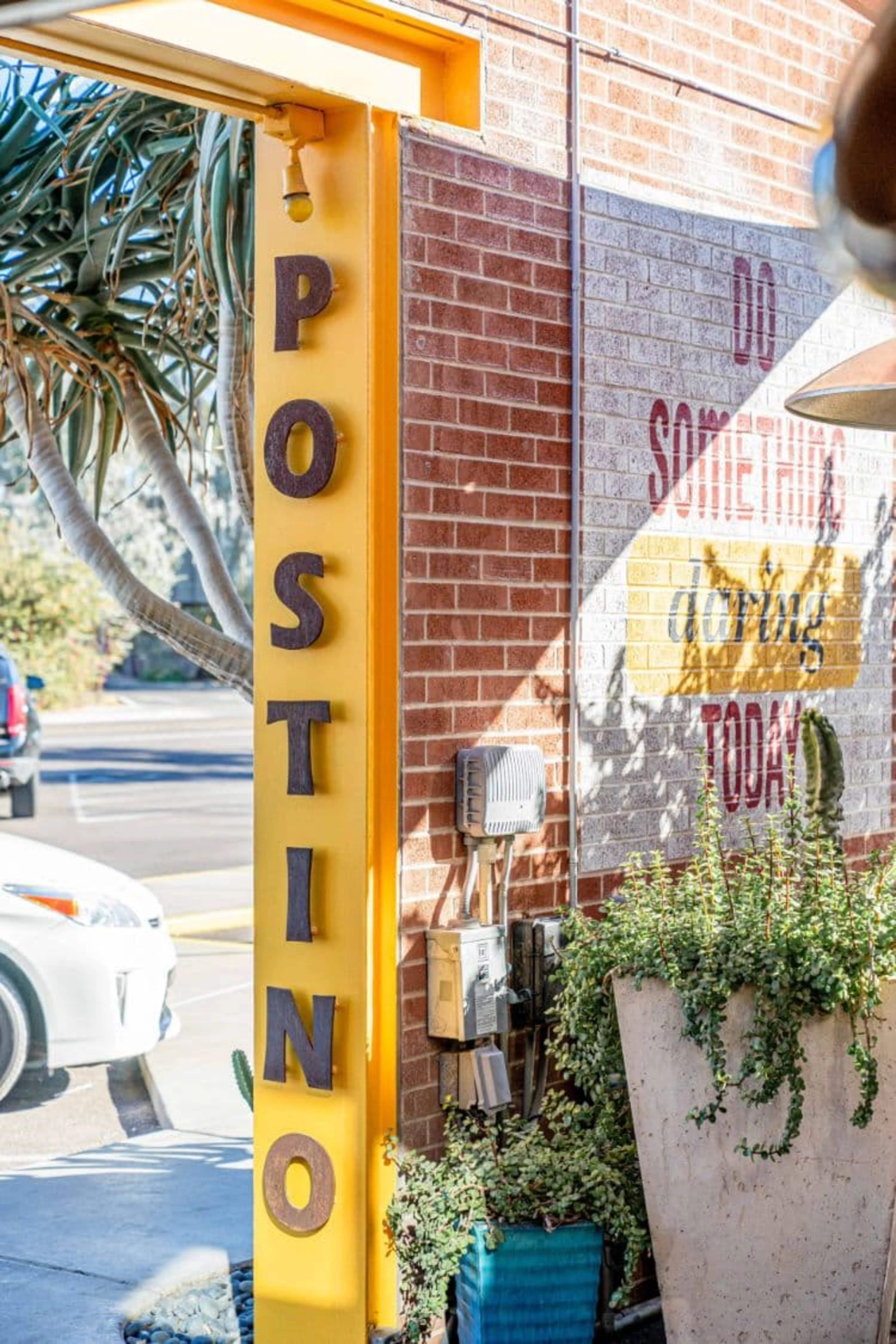 Yellow door frame with the word Postino and some plants.