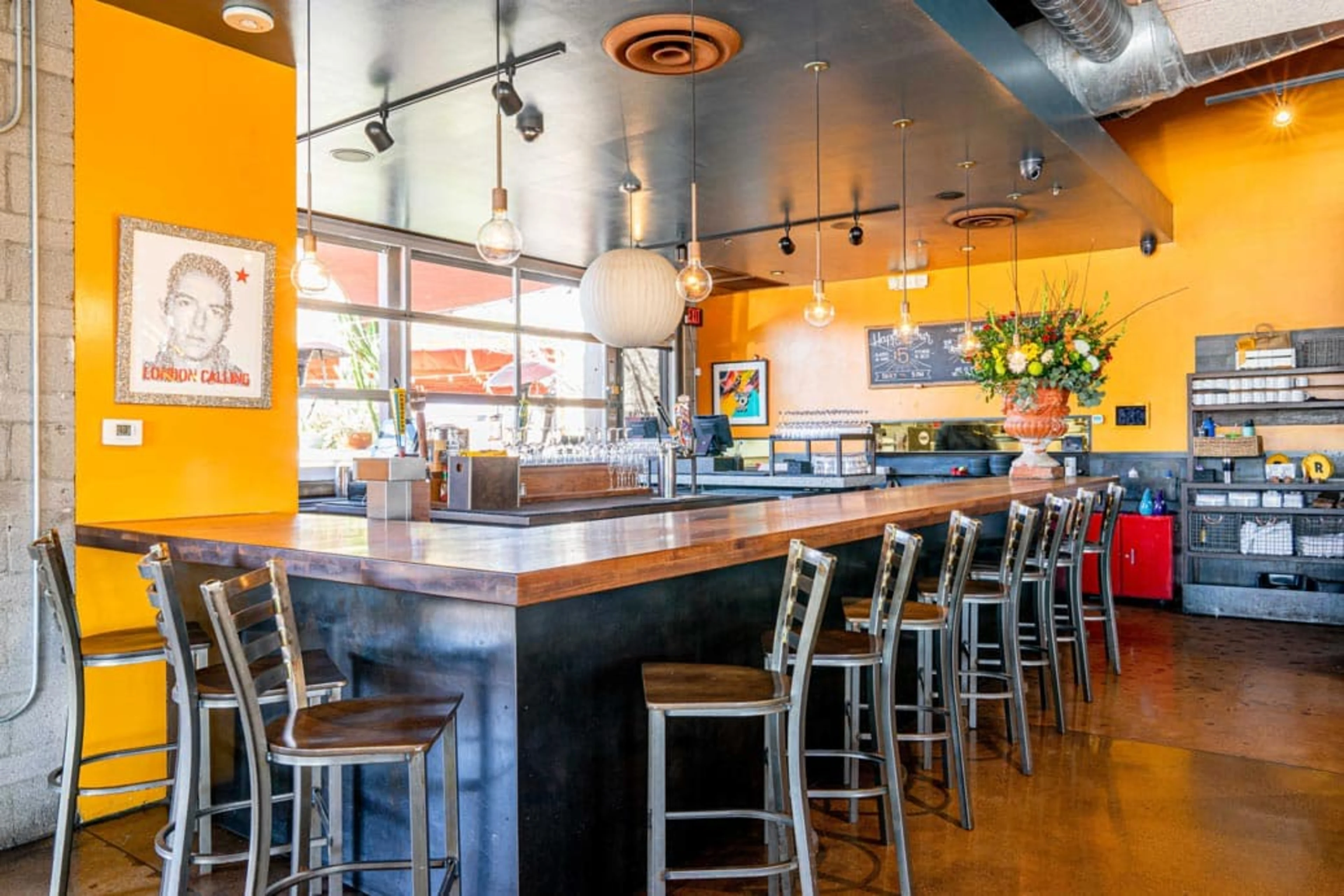 A long bar with high top chairs and yellow walls.