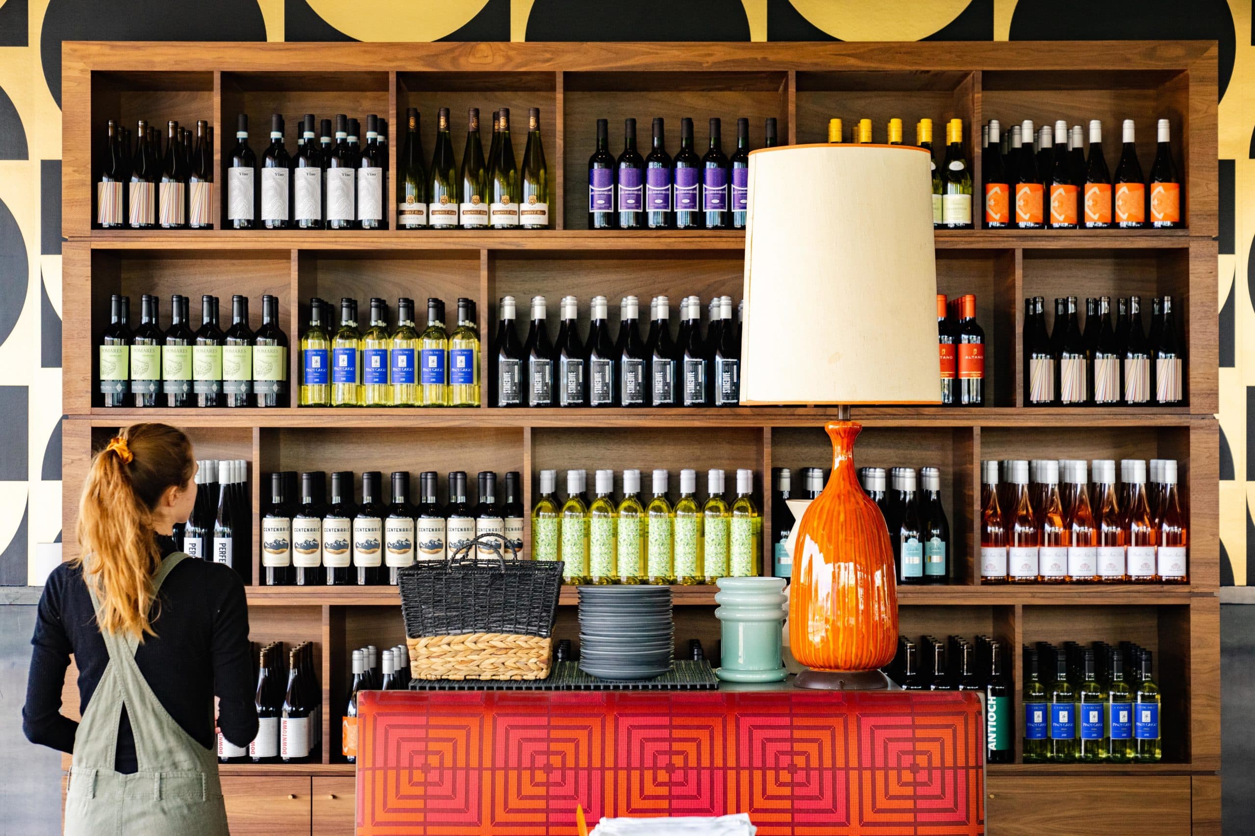 A large shelf filled with wine bottles and a woman examining them. 