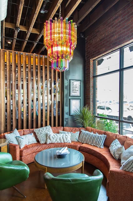 A large room with a round coffee table, large orange couch, green chairs, and a colorful glass chandelier