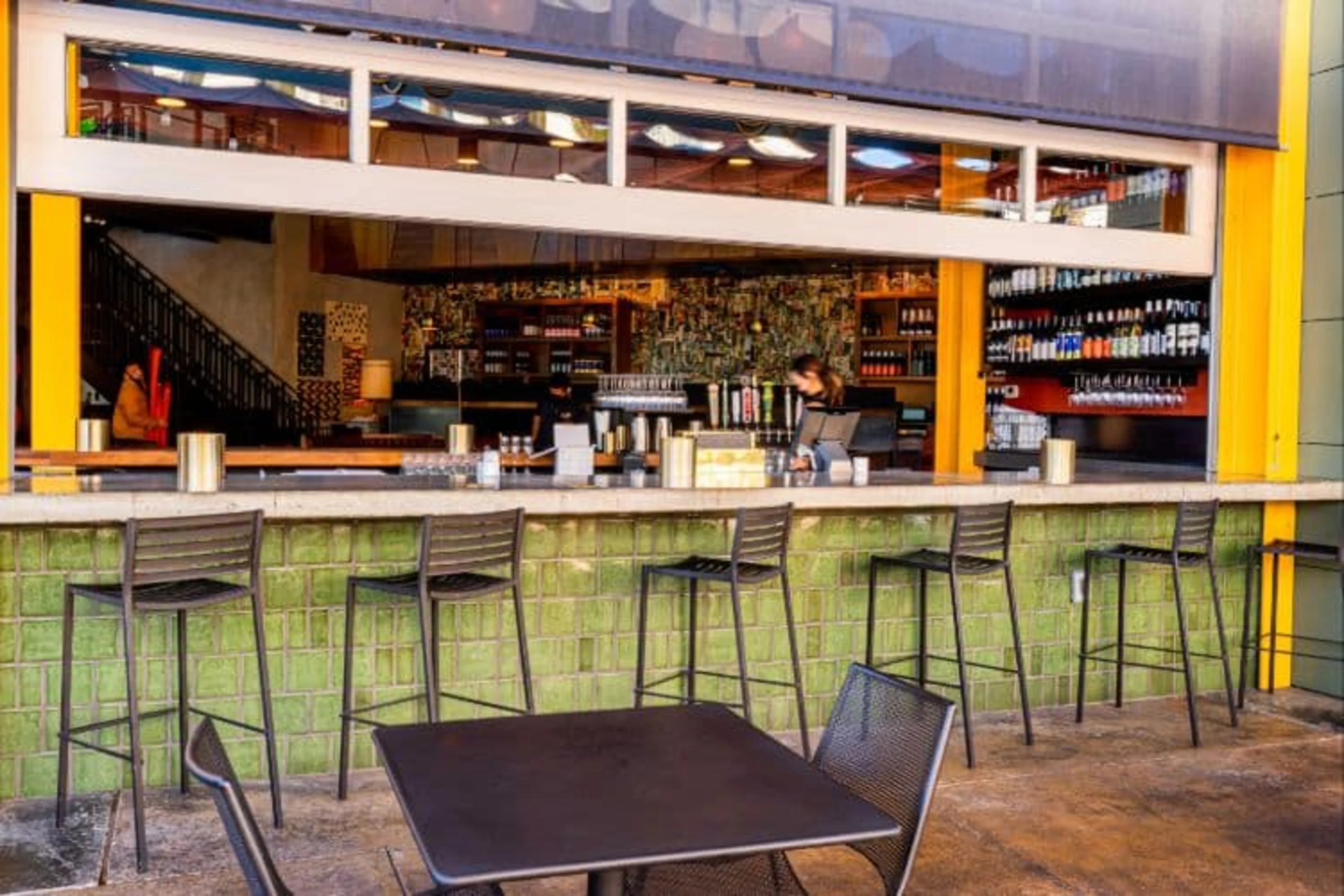 A green outdoor bar patio with high top chairs.