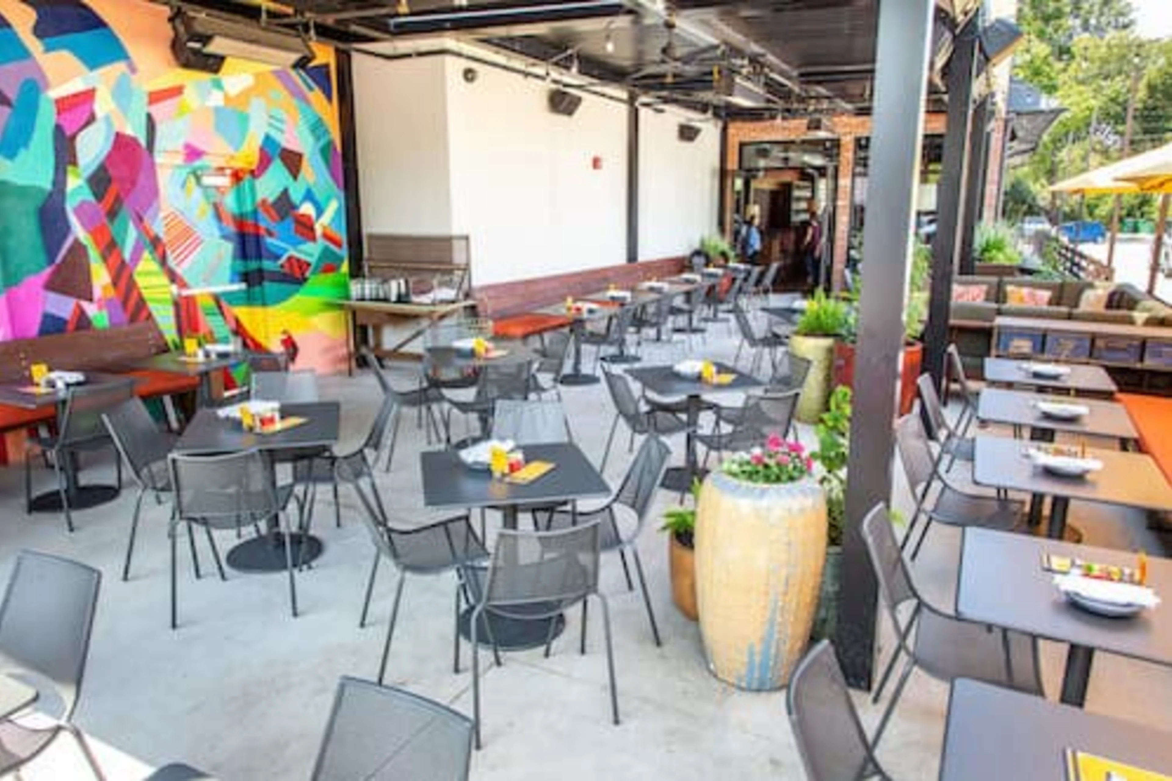 An empty patio with many tables and a colorful mural on the wall.