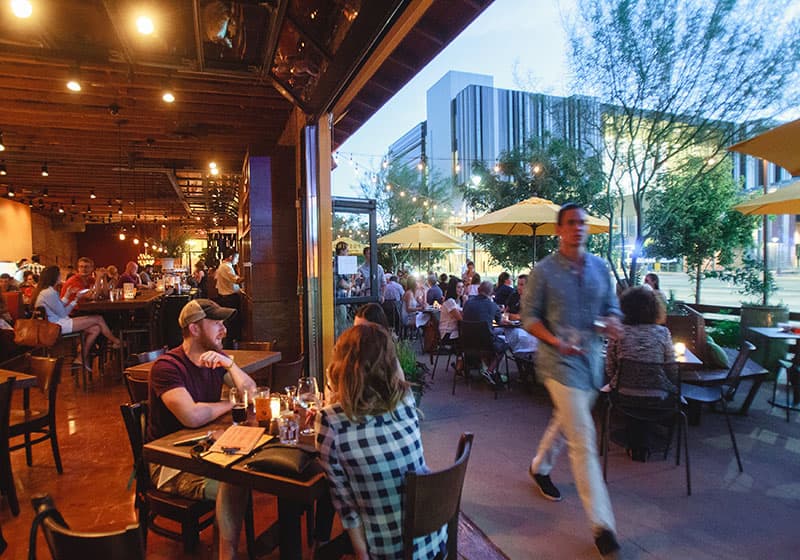 Restaurant at dusk with patrons and a waiter walking on the patio.