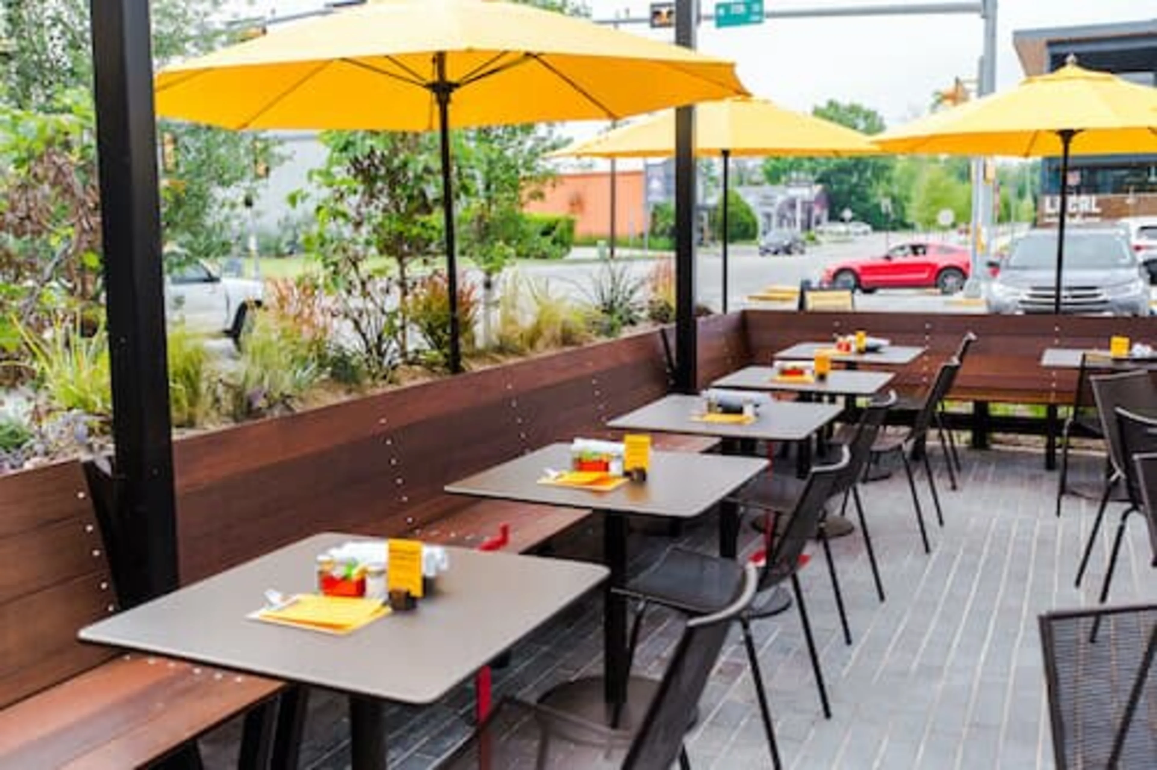 A long wooden bench with tables and yellow umbrellas.