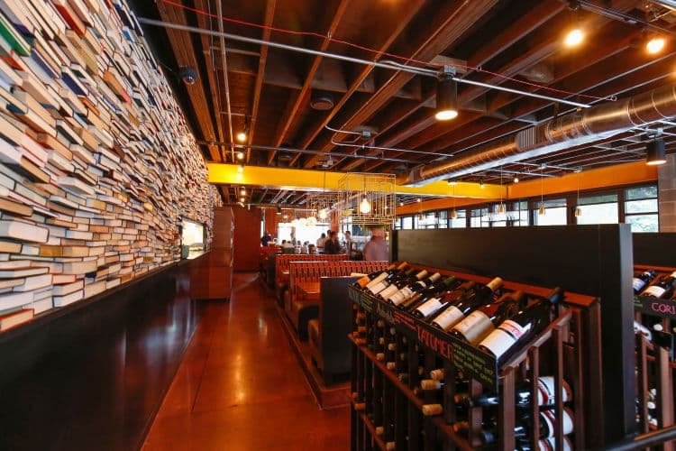 Wall of colorful stacked books near wine displays.