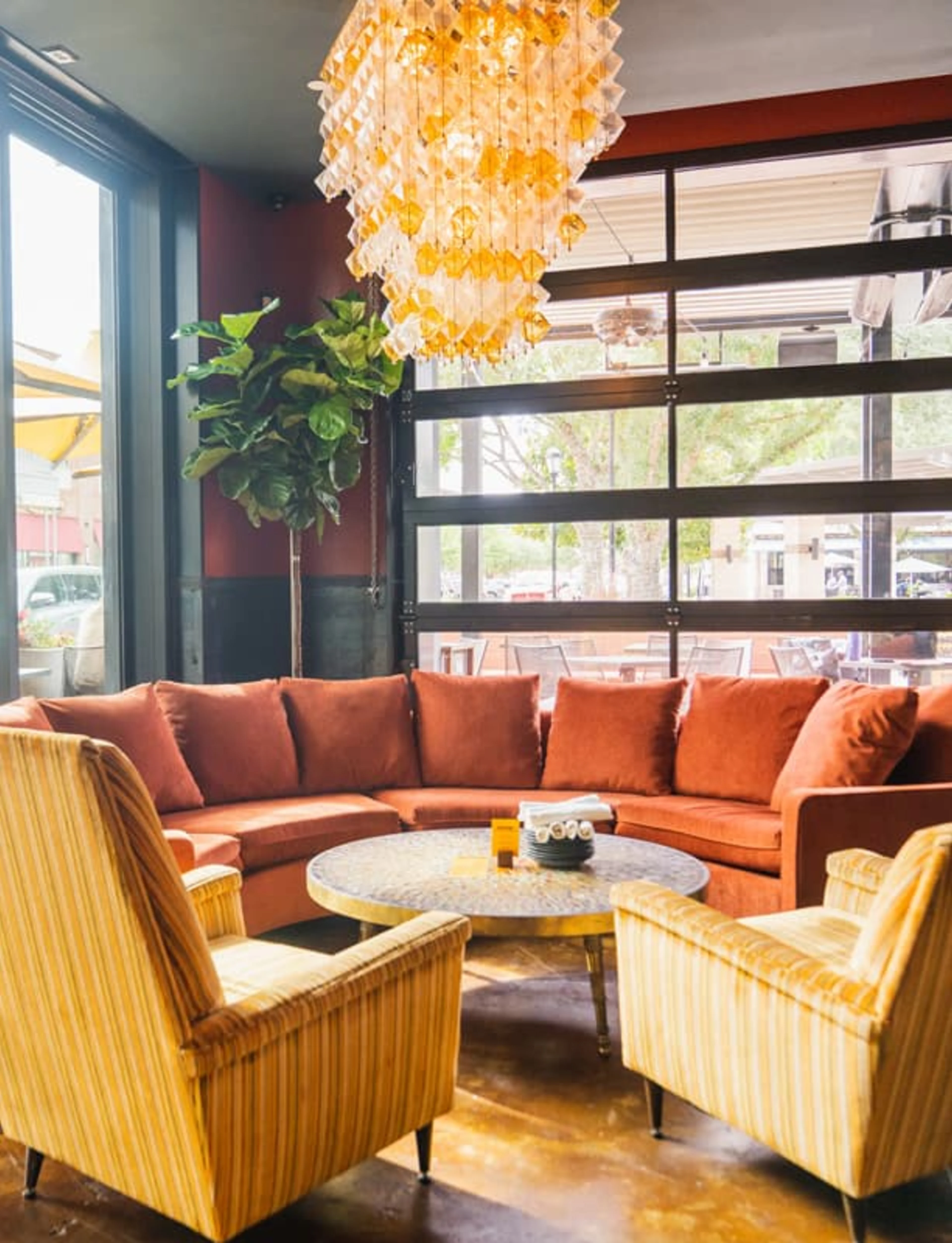 A large orange couch with a large glass chandelier above it.