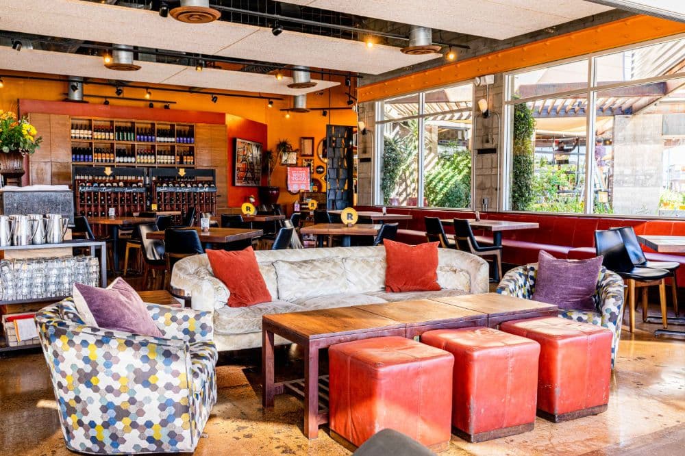 A sofa, chairs, and red stools surround a wooden table.