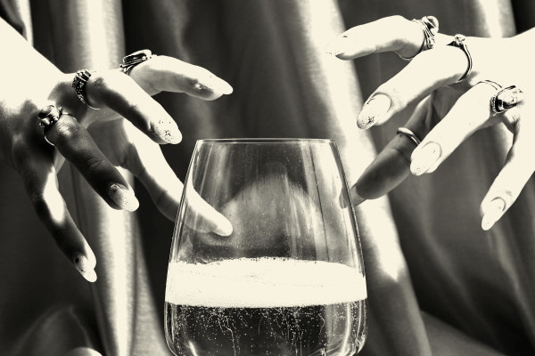 Black and white photo of two hands hovering over a wine glass, like it's a crystal ball