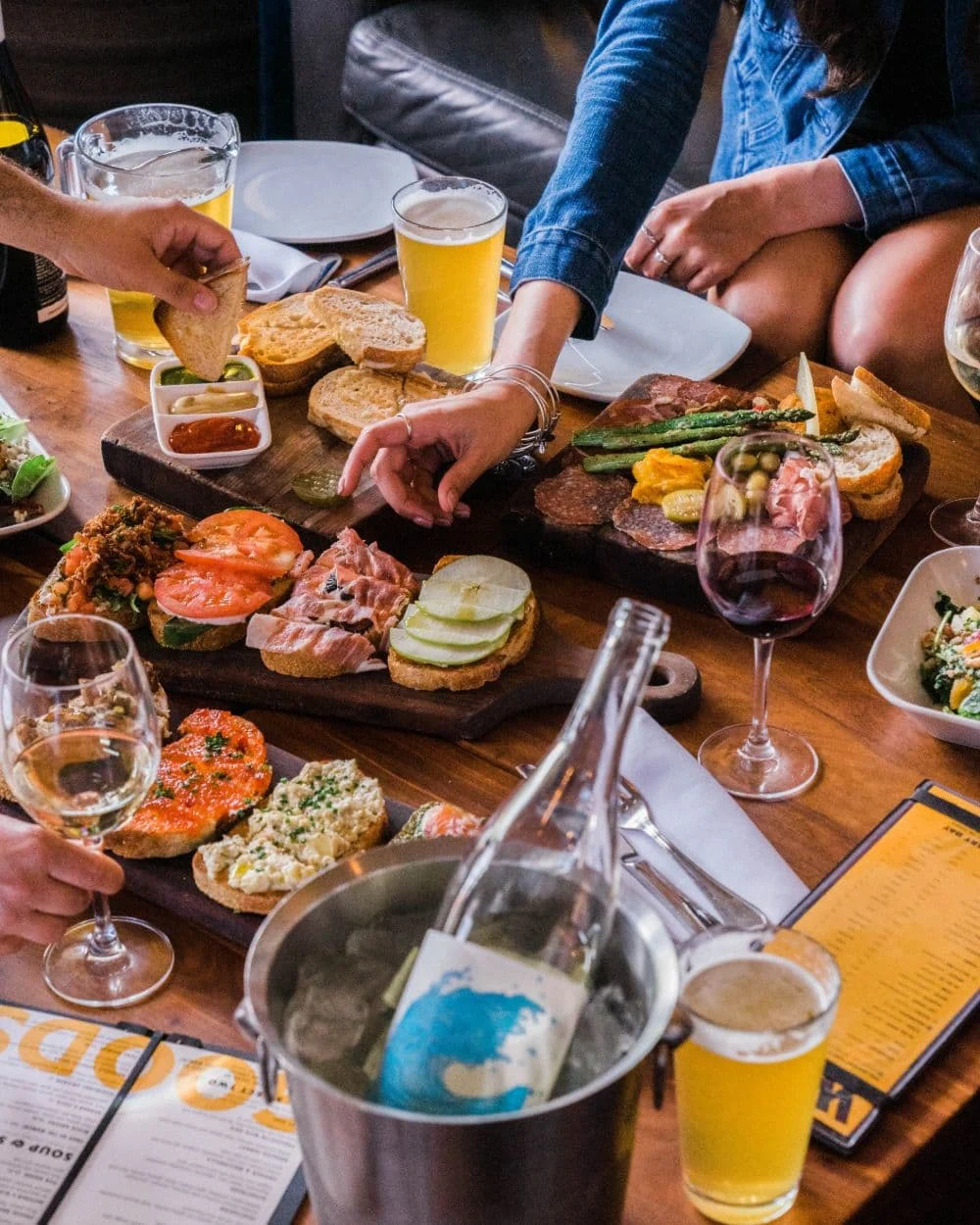 A table full of food and wine glasses with people reaching for the food.