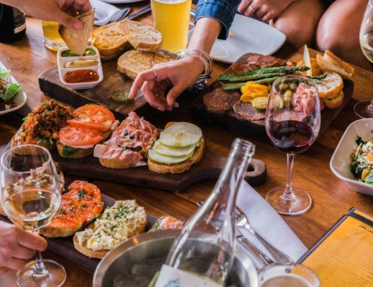 A table full of food and wine glasses with people reaching for the food.