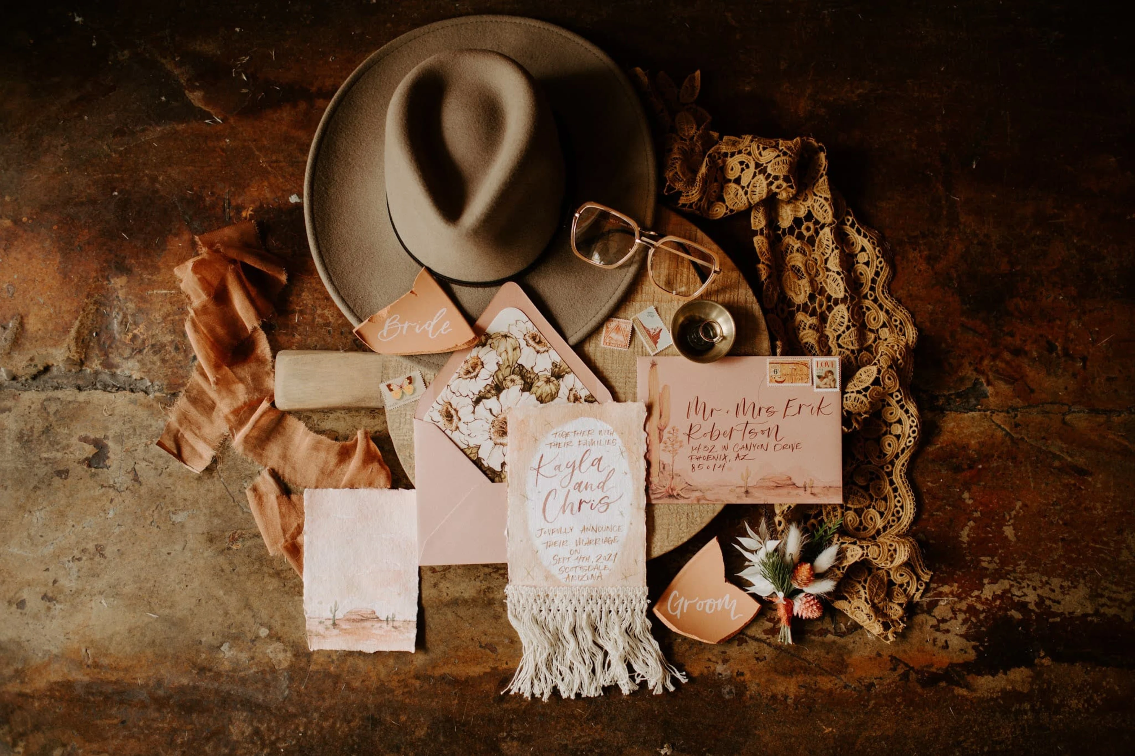 A wedding invitation surrounded by a hat, scarf, and flowers.