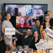 A group of people posing with signs in front of a zoom meeting on a screen.