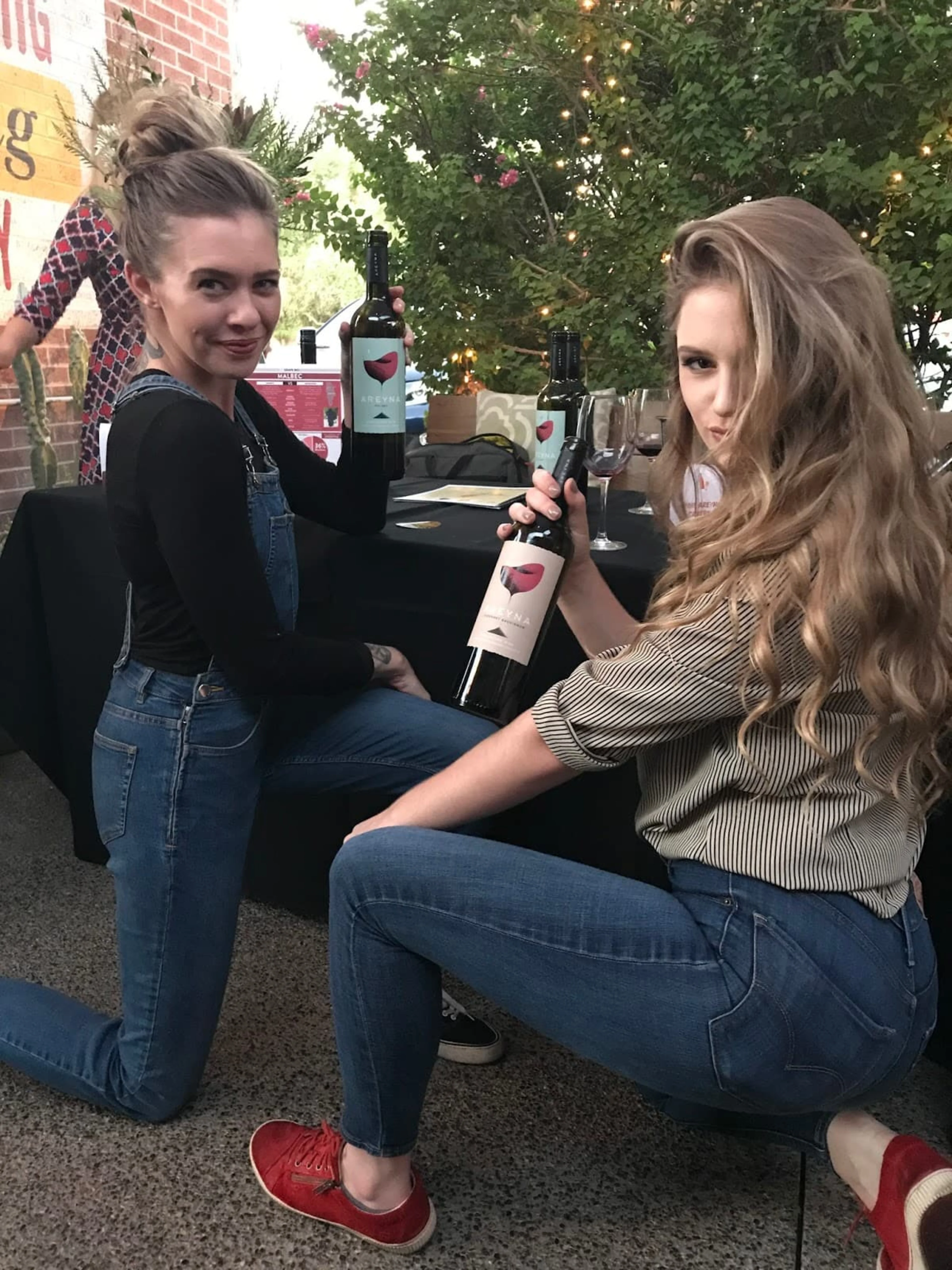 Two women hold up wine bottles and pose.