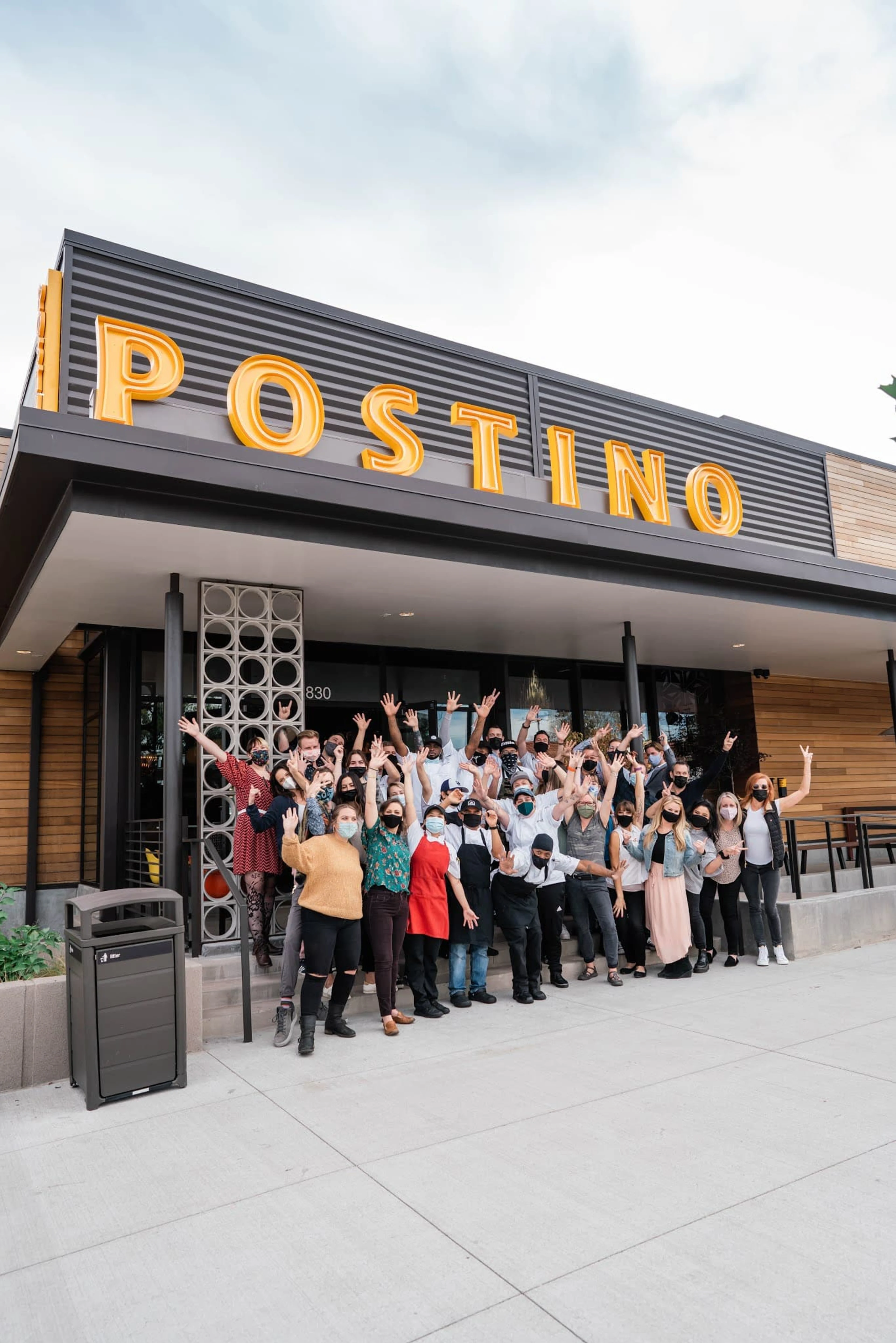 A group of people holding up their hands in front of Postino restaurant.