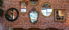 Brick wall with six mirrors mounted on it with a large brown sofa below. 