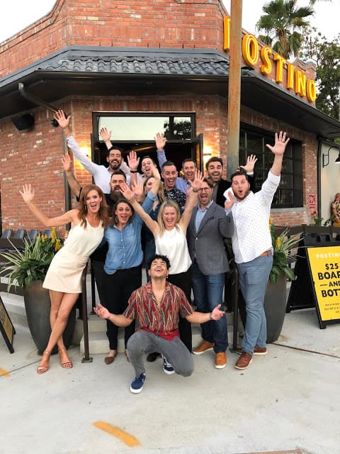 A group of people standing in from of a Postino with their hands in the air