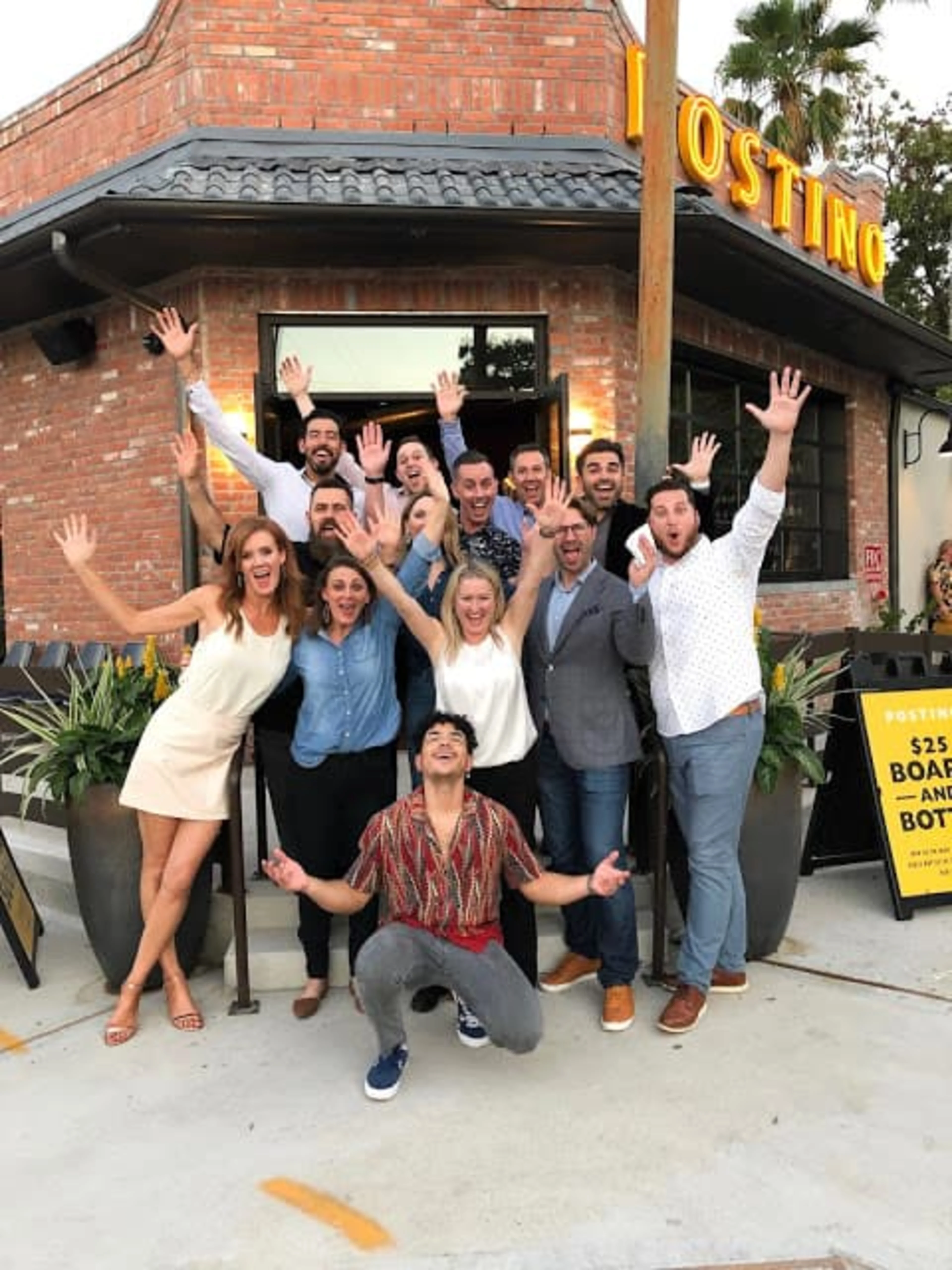A group of people standing in from of a Postino with their hands in the air