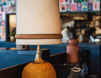 A brown and tan lamp on a table with a colorful wall behind it.