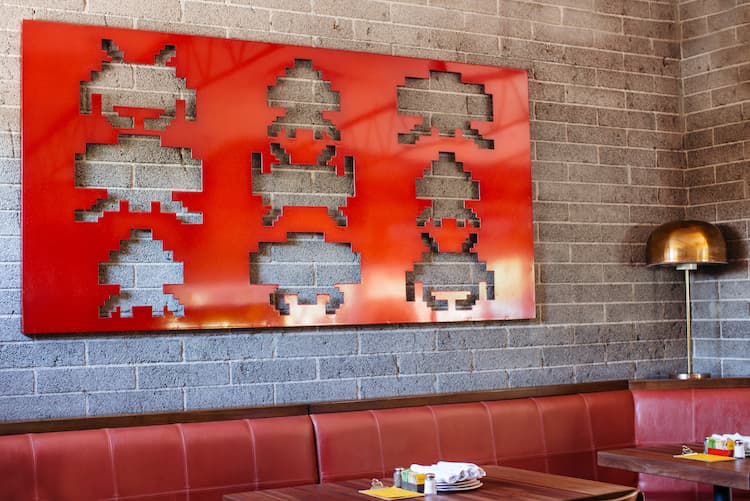 A long red leather restaurant bench with a large red paining overhead.
