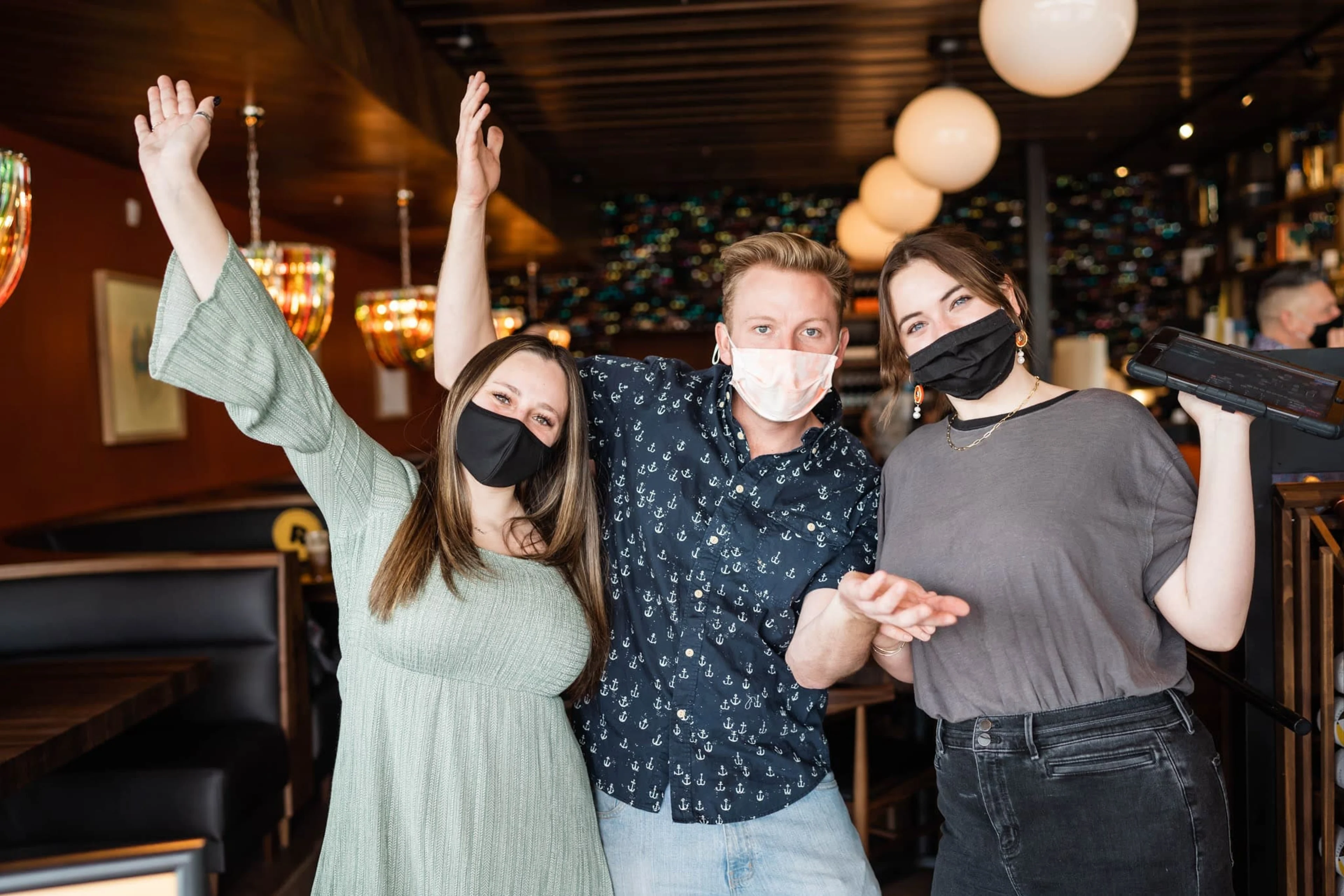 Three people wearing masks pose together with arms up