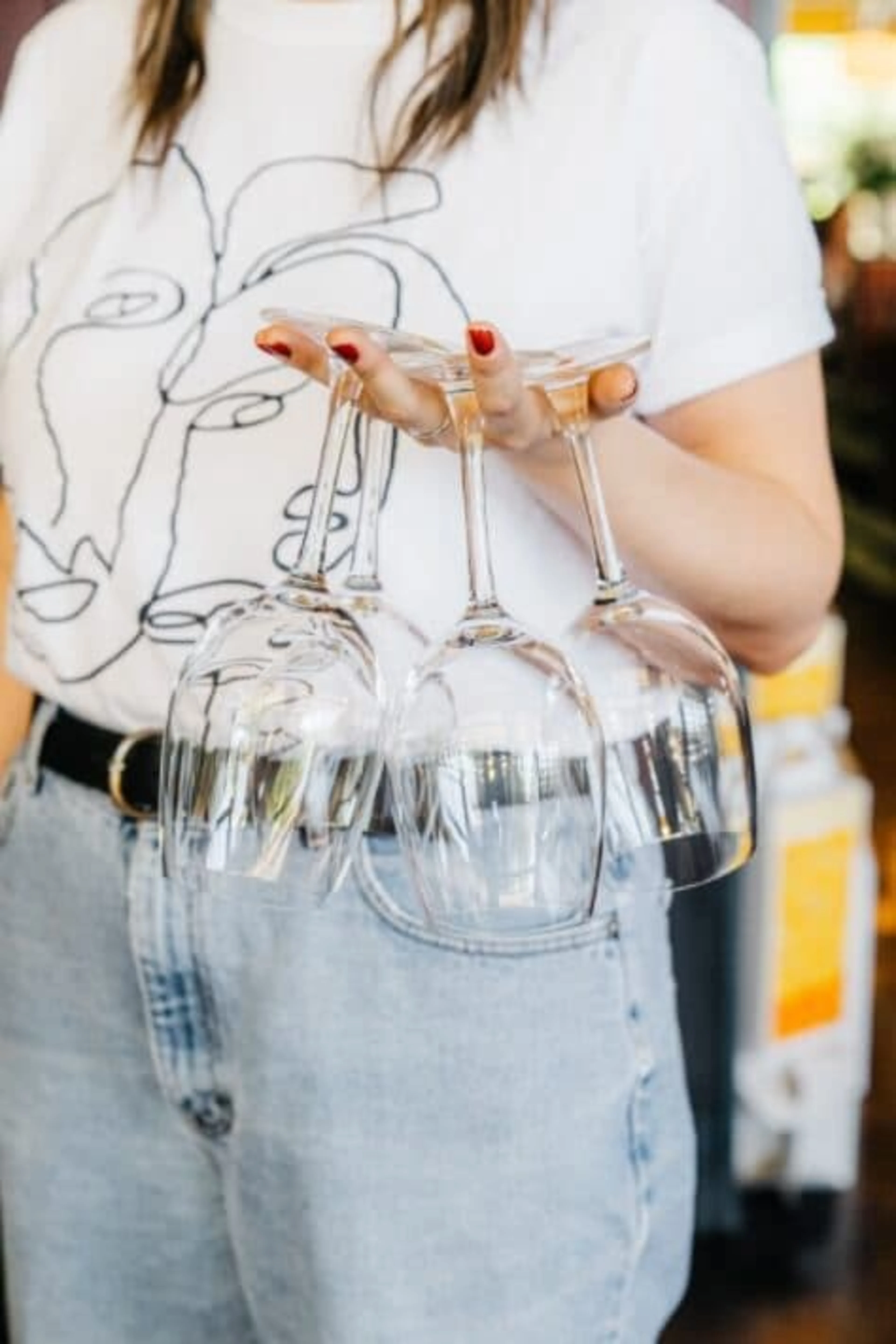 A woman holding three wine glasses with her fingers.