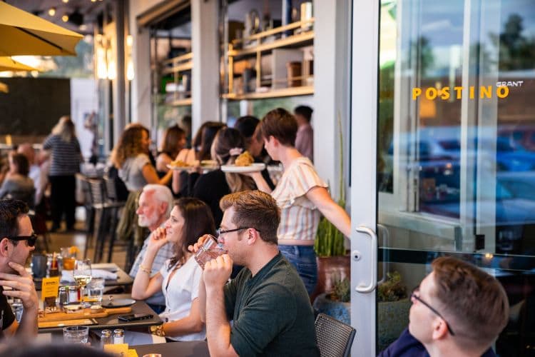 A busy restaurant patio with diners and a waitress carrying a tray.