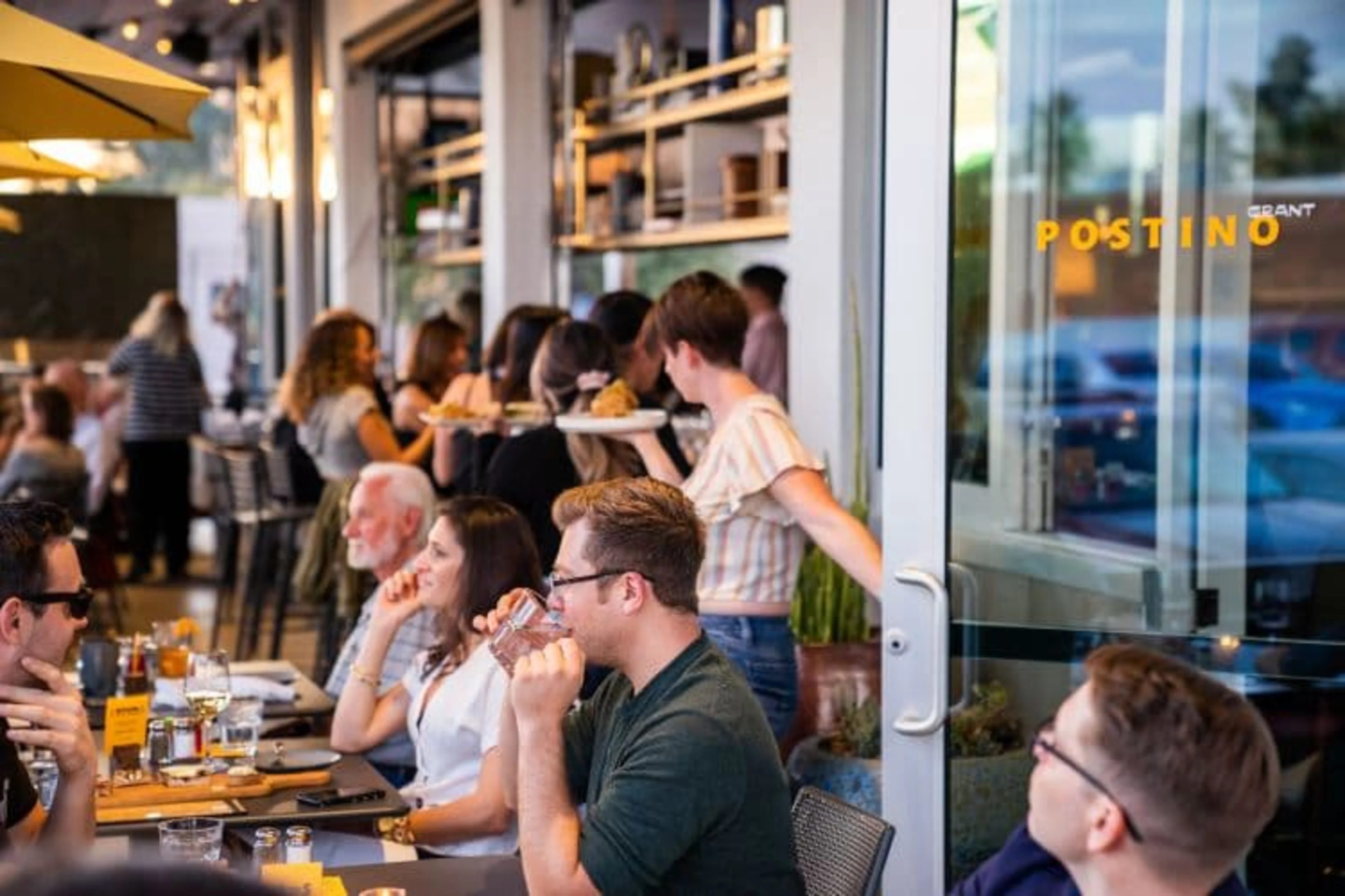 A busy restaurant patio with diners and a waitress carrying a tray.