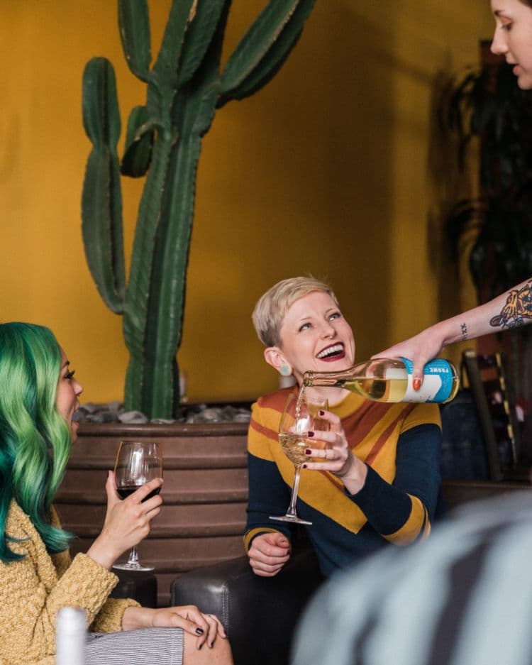 Two women are being served wine and smiling.