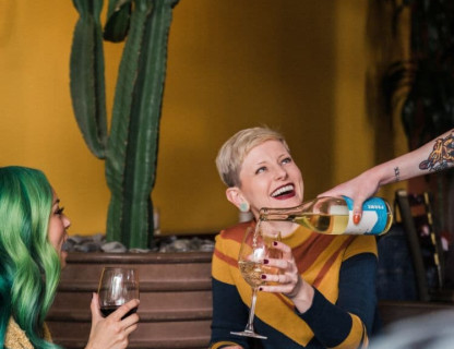 Two women are being served wine and smiling.