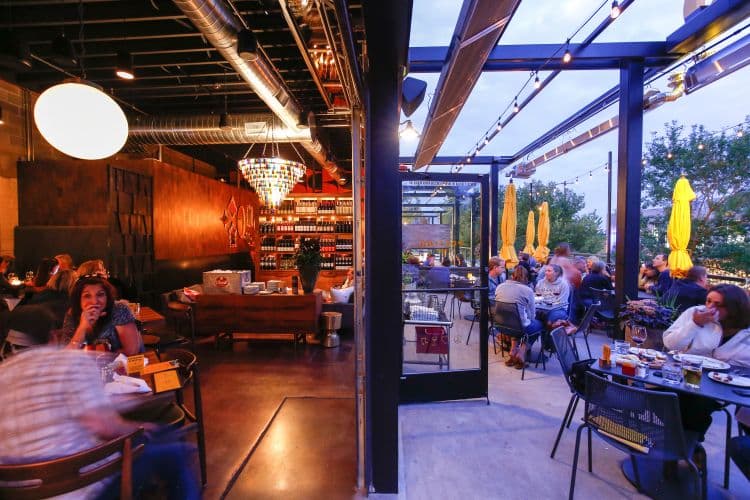 Inside and outside of a restaurant with tables of people.
