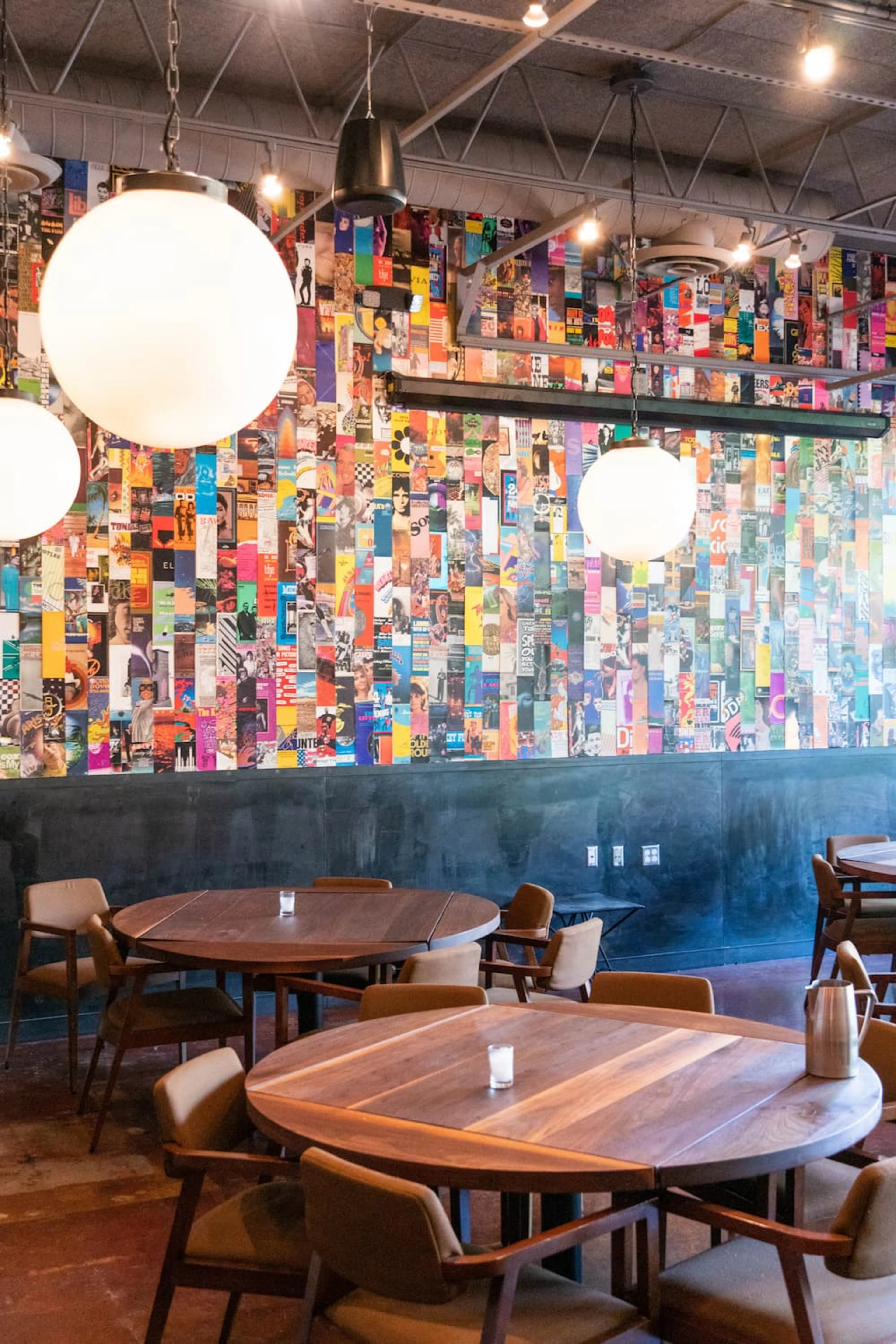 A colorful wall with round lights hanging above wooden tables.