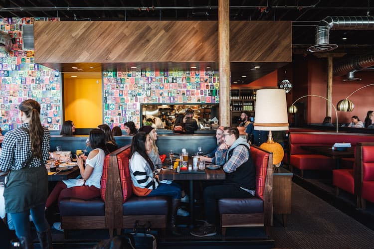 Red restaurant booths full of patrons with a colorful wall behind them. 
