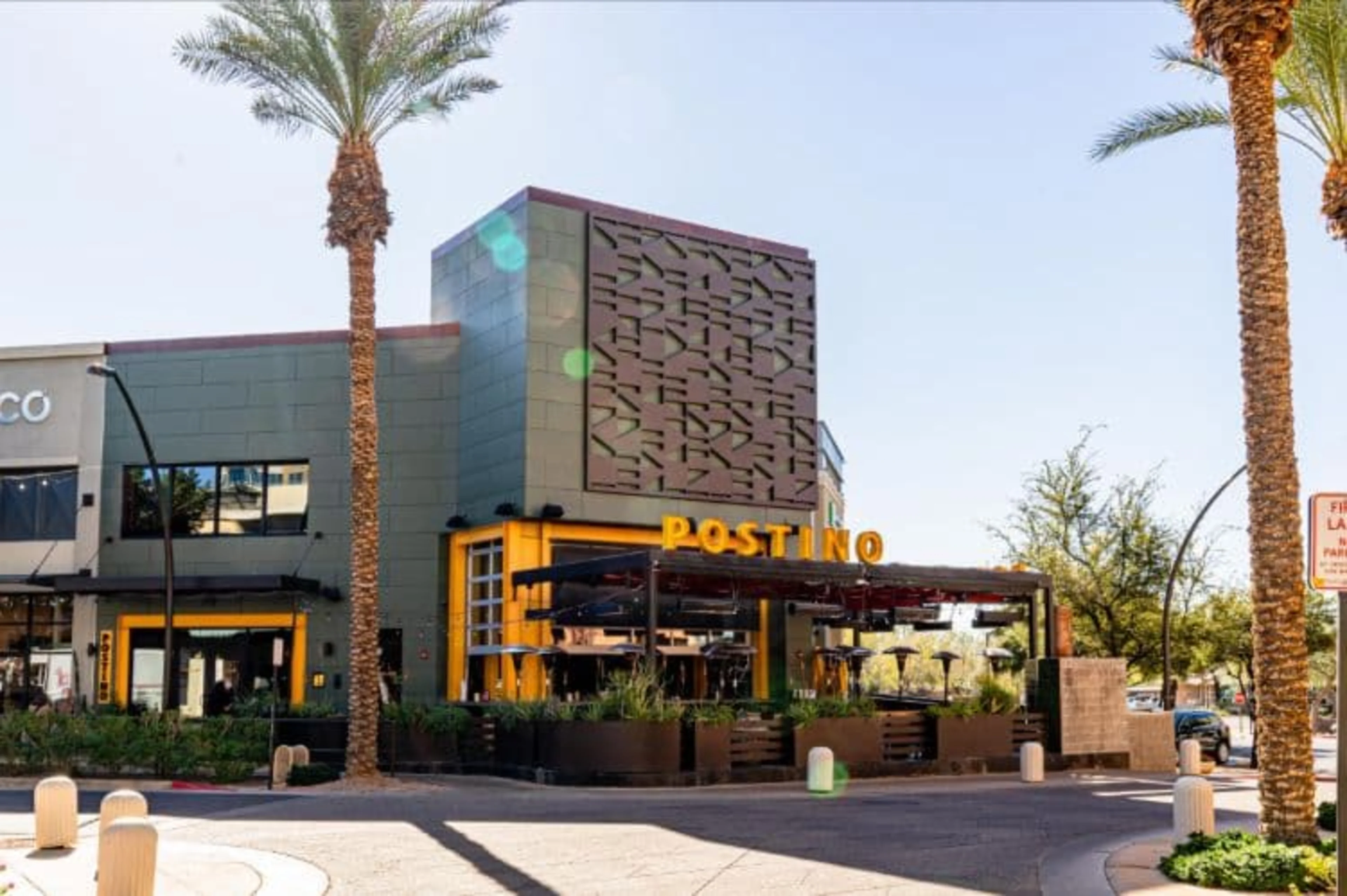 The exterior of a building with palm trees and a large yellow Postino sign.