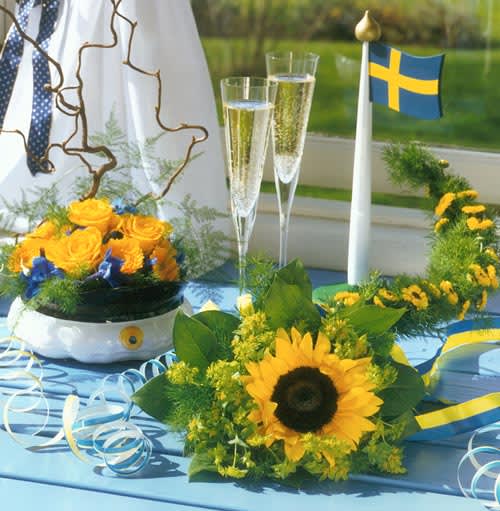 Det är härligt att hänga blommor om halsen på en student! Den här buketten har fått en blomstersvans som effektfullt vilar mot studentens axel. I svansen finns små krysantemum och grönt, buketten i övrigt är komponerad av en solros, daggkåpa och vaktelbär ("salal"). I studentmössan av porslin finns gula rosor och minigerbera, blåa riddarsporrar och grenar av ormhassel. Florist: Mikael Olsson. Foto: Tommy Durath.