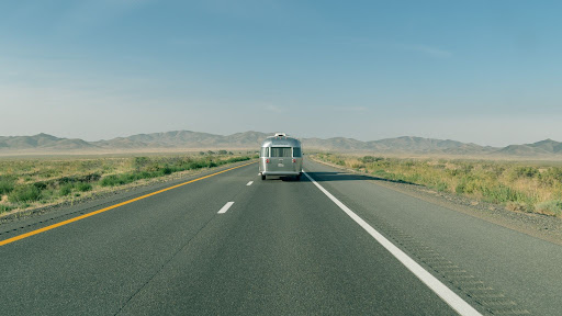 A rear photo of an RV driving down a long, empty desert road. 
