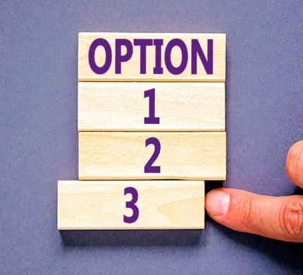 Hand placing wooden blocks labeled "OPTION 1 2 3" in a stack against a purple background.