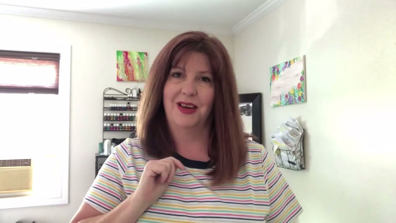 Person with shoulder-length hair wearing a striped shirt standing in a room with light-colored walls — background includes air conditioning unit, colorful wall art, mirror, and organized papers, suggesting a home office or personal workspace.