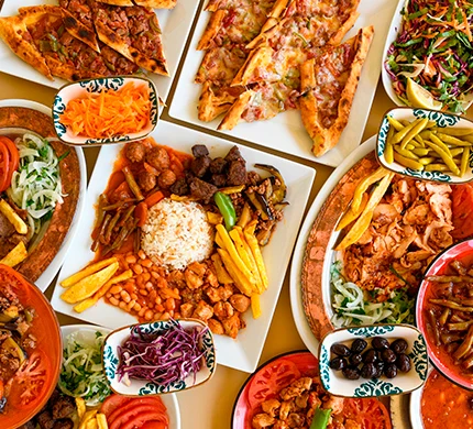 Assortment of Turkish dishes including flatbread pizzas, meat platters with rice, and colorful side dishes on decorative plates.